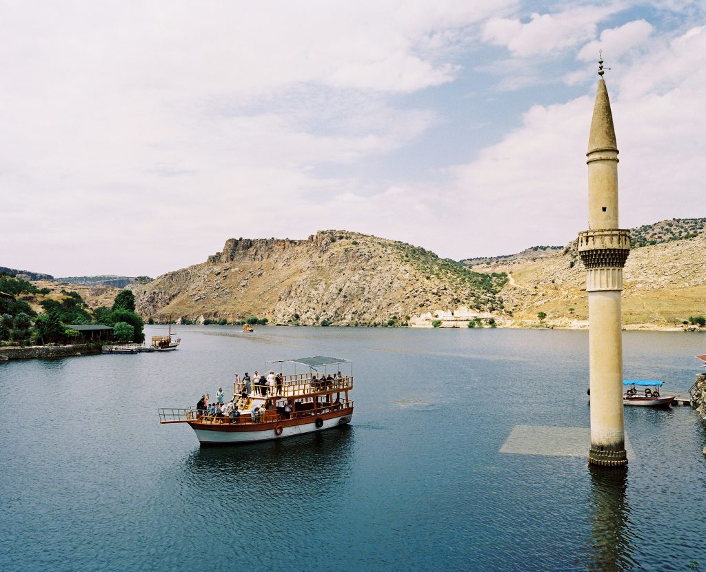 A tourist boat tour is visiting the former Savaçan Village flooded by the reservoir lake of the Birecik Dam on the Euphrates river in the late 90's. The town was among those settlements, ancient and contemporary, that would remain under the rising water levels of the local dams and rivers following the execution of the GAP project. Until the area was flooded in 1999, the people lived from fishing in the Euphrates and farming on the riverbank. Savaçan, Turkey